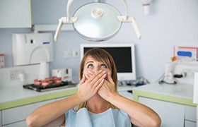 anxious woman sitting in dental chair and covering mouth with hands